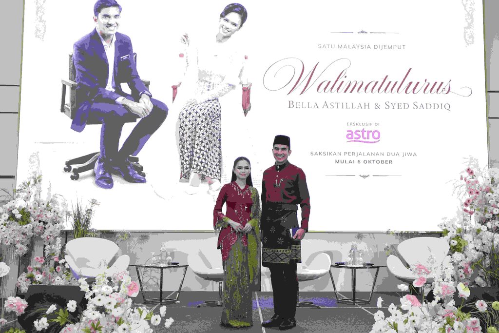Bella Astillah dan Syed Saddiq berpakaian tradisional sedondon berdiri di hadapan poster pelancaran siri Walimatulurus Astro