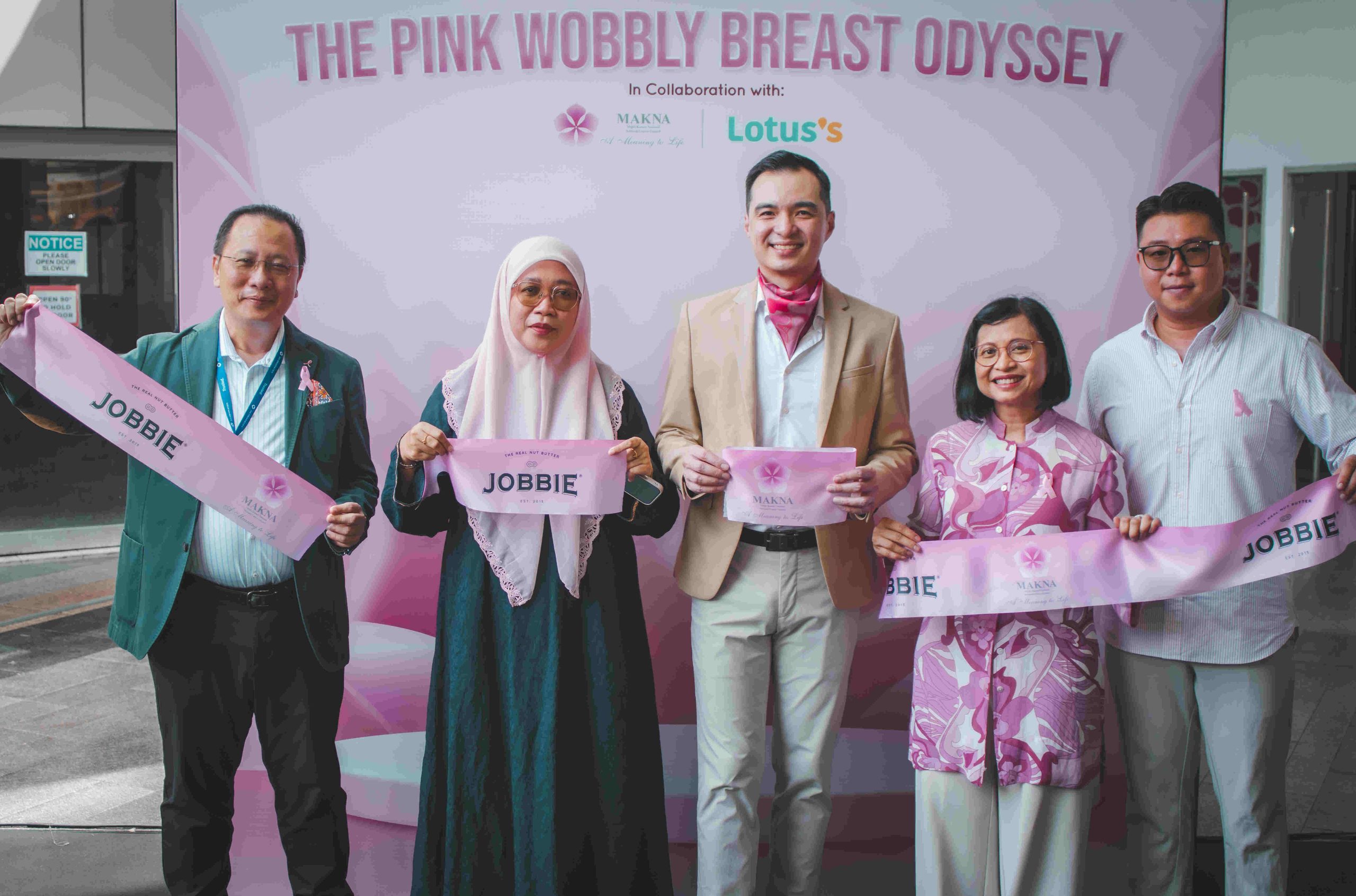 Barisan wakil Lotus's, MAKNA dan JOBBIE memegang sepanduk fabrik merah jambu The Pink Wobbly Breast Odyssey di majlis pelancaran