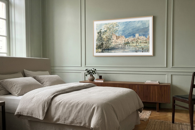A Samsung The Frame TV showcasing a landscape painting from the Samsung Art Store collection mounted on a bedroom wall